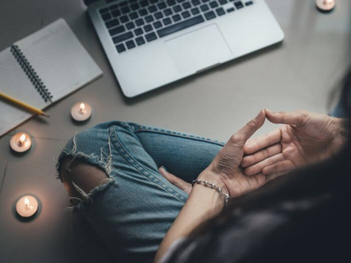 Person sat on the floor cross-legged in front of an open laptop, surrounded by a note book and tealight candles.