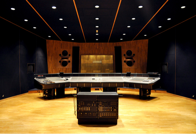 Large, modern, empty recording studio. The mixing desk is facing the booth.