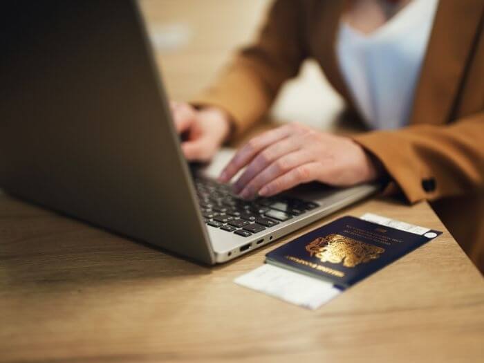 A close up of a woman sitting at a laptop with a passport on the table.