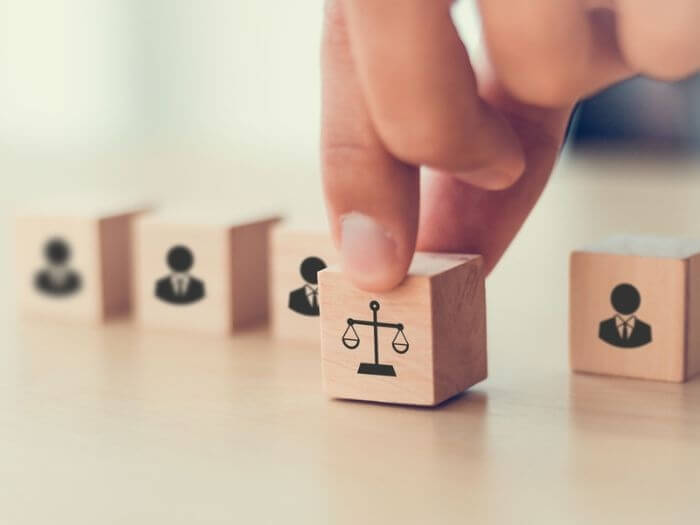 Five wooden blocks with the outline of people apart from one which is a weighing scales, representing fair work.
