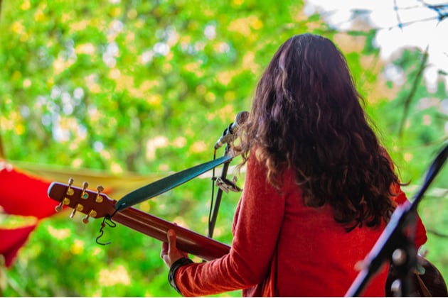 Back of a women playing acoustic guitar on an outdoor stage.