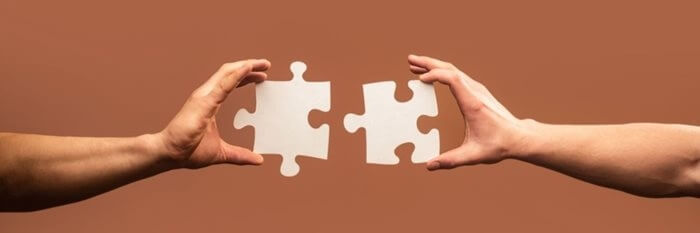 Two hands outstretched, each holding a jigsaw piece that will fit together.