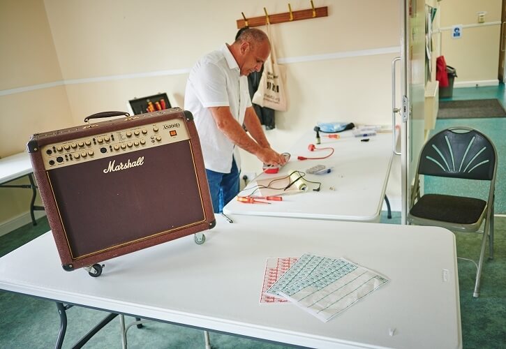 Mike Nottage stands behind a table set up for PAT testing with a medium sized amp on display