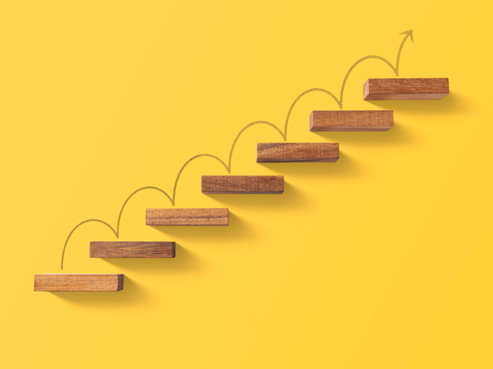 Wooden steps on a bright yellow back ground, an arrow is draw over them upwards, to represet the concept of personal development and improvement.