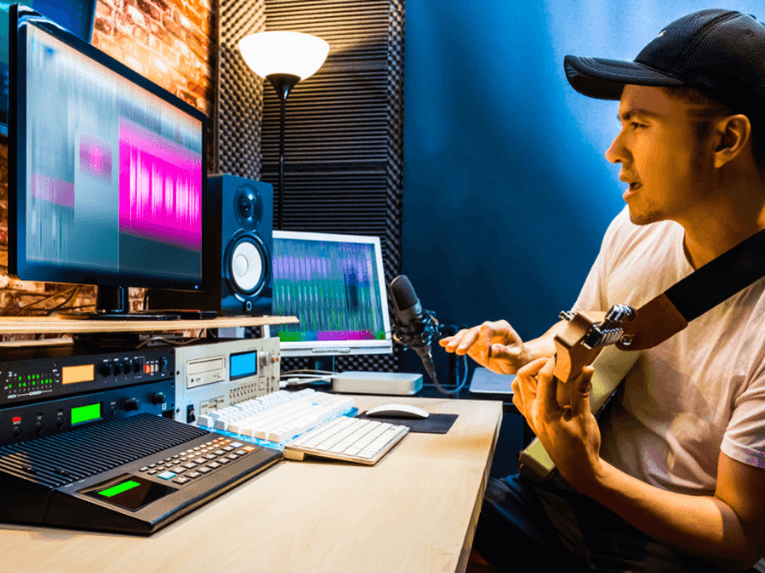 Young male musician sat in front of home studio with guitar.