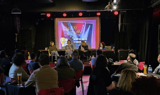 Belfast event with a crowd watching the panellists on stage. Behind them a projector says 'Fair Play on Tour 2023' with the MU logo.