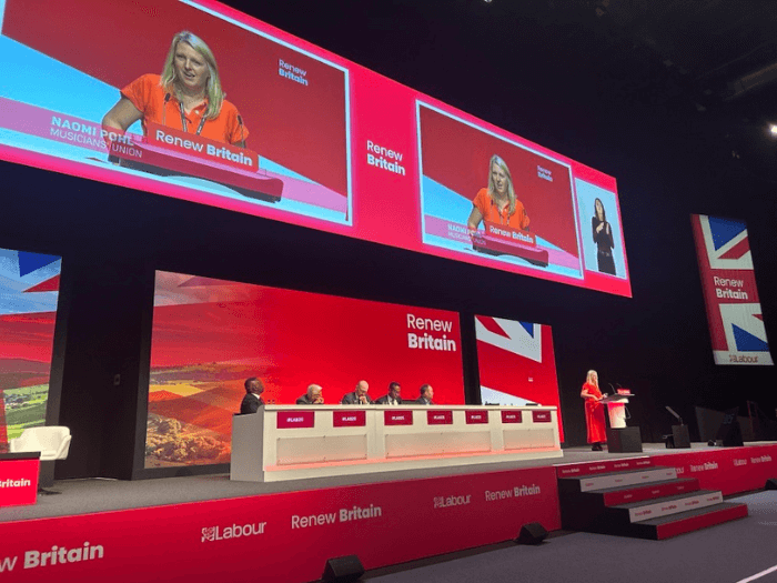 Naomi Pohl speaking on stage at a Labour Party Conference 2025.