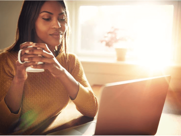 Young women sat at an open laptop at home, holding a mug